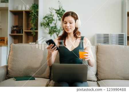 Happy woman with headphones using a laptop in a cozy living room with food and drink. Perfect for themes 123990488