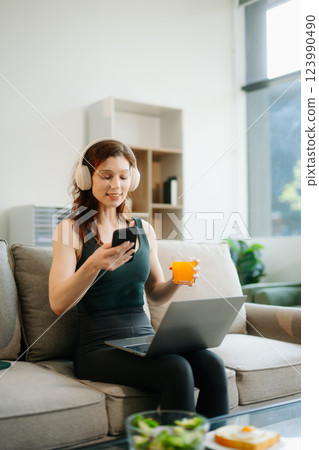 Happy woman with headphones using a laptop in a cozy living room with food and drink. Perfect for themes Happy woman with headphones using a laptop in a cozy living room with food and drink. Perfect for themes 123990490