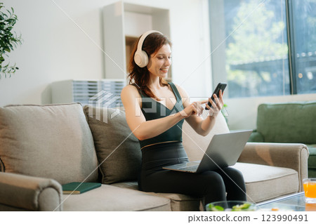 Happy woman with headphones using a laptop in a cozy living room with food and drink. Perfect for themes 123990491