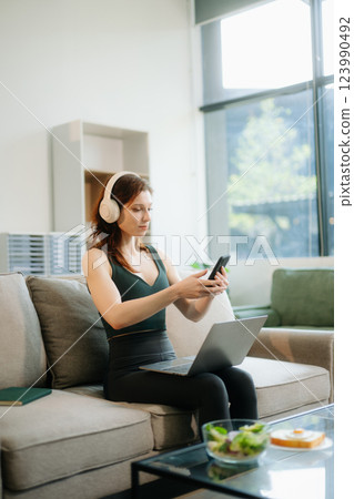 Happy woman with headphones using a laptop in a cozy living room with food and drink. Perfect for themes Happy woman with headphones using a laptop in a cozy living room with food and drink. Perfect for themes 123990492