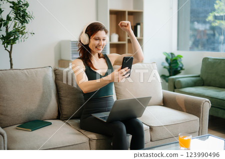Happy woman with headphones using a laptop in a cozy living room with food and drink. Perfect for themes Happy woman with headphones using a laptop in a cozy living room with food and drink. Perfect for themes 123990496