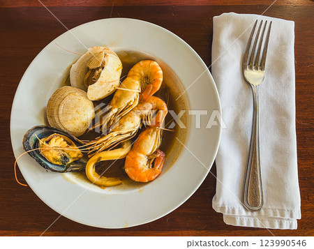 Seafood soup in a white plate on a wooden table. 123990546