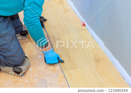 Contractor carefully cuts laminate flooring planks to fit in living room during home renovation work. 123990584