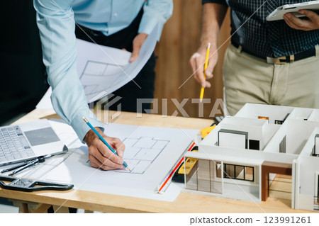 Professional collaboration in architecture. Two engineers work on construction plans, using tools like laptops, tablets, and scale models. 123991261