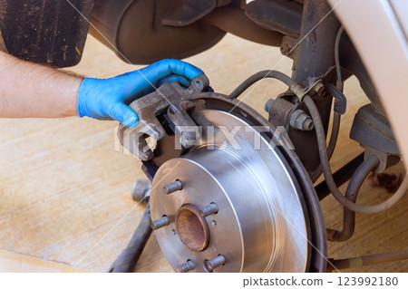 Technician replaces worn brake pads on car in well lit garage while wearing protective gloves. Technician replaces worn brake pads on car in well lit garage while wearing protective gloves. 123992180
