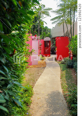 Tropical garden pathways lead to colorful structures, blending nature and aesthetic charm. 123992420