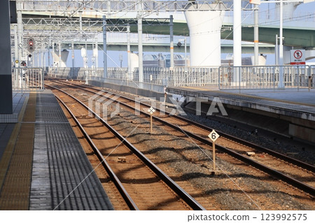 A view of a cityscape with railroad tracks, blue sky and highway bridge legs as seen from a station platform 123992575