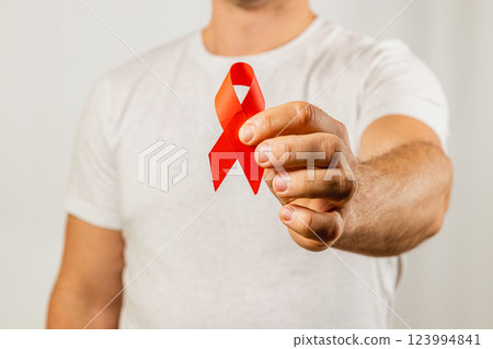 Man holding a red ribbon to raise awareness for AIDS prevention and support 123994841