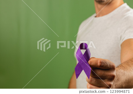 Person holding a purple ribbon against a green background to raise awareness 123994871