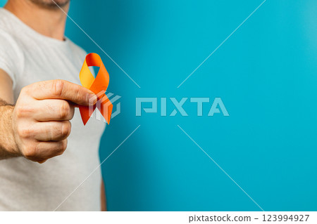 Person holds orange ribbon for mental health on blue background 123994927
