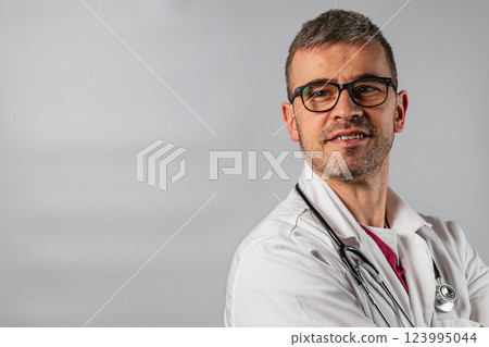Confident doctor in white coat standing with stethoscope in studio Confident doctor in white coat standing with stethoscope in studio 123995044