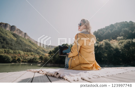 Woman in Yellow Jacket Working on Laptop by Lake 123997748