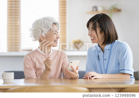 護理人員用智慧型手機與一位老年婦女交談 護理人員用智慧型手機與一位老年婦女交談 123998096