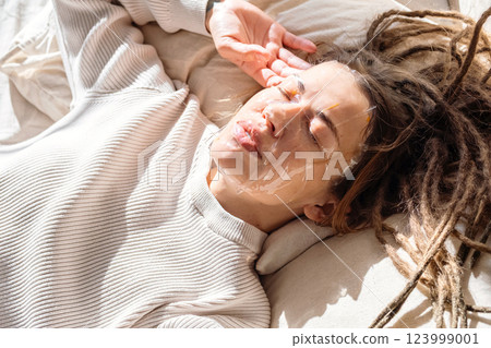Woman Having Facial Mask While Resting On Bed. 123999001