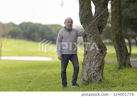 Senior man leaning against a cork oak tree in a green park 124001778