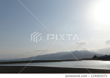 A springtime hazy blue sky, rolling mountains, and a seaside estuary reflecting the evening light 124002072