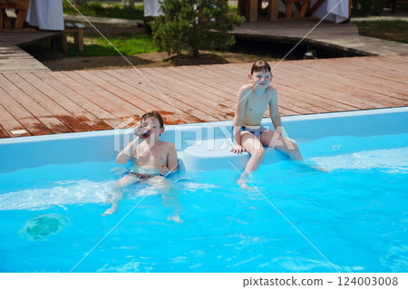Two boys with a bottle of soda playing and swimming in the pool.  124003008
