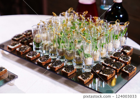 tray with sandwiches with black caviar and cups with canapes and white sauce. 124003033
