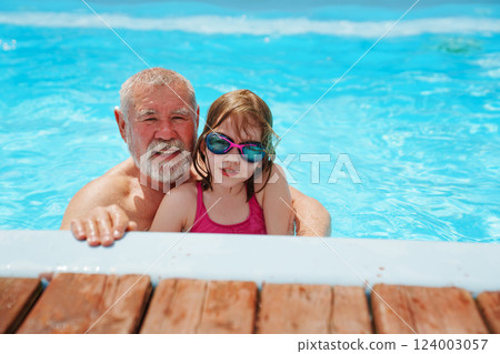 A grandfather and granddaughter play and swim in an outdoor pool. A grandfather and granddaughter play and swim in an outdoor pool. 124003057
