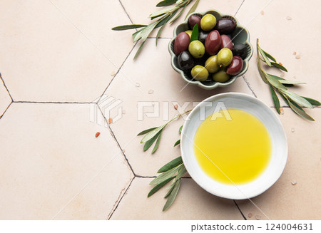 Olive oil and olives with olive branches resting on a tiled surface Olive oil and olives with olive branches resting on a tiled surface 124004631