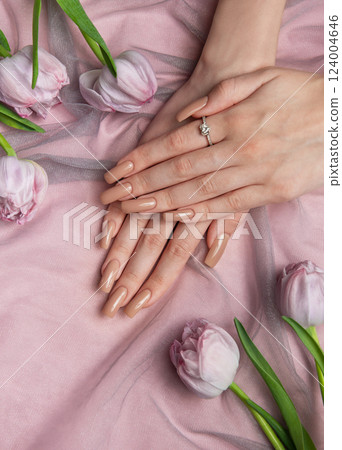 Woman showing nude manicure with engagement ring near pink tulips 124004646