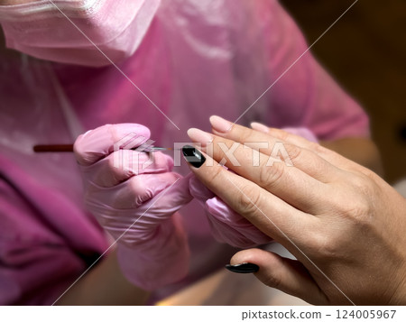 Female hand receiving manicure with black and pink nail polish 124005967