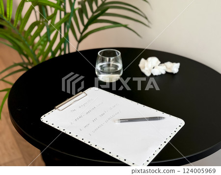 Empty table with black circular top, clipboard, crumpled papers, and glass of water Empty table with black circular top, clipboard, crumpled papers, and glass of water 124005969