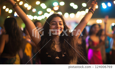 Joyful Indian woman dancing, arms raised high, celebrating amid colorful festive lights and energetic nighttime crowd 124006769