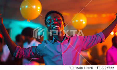 Energetic male celebrating at vibrant party, raising arms while dancing, surrounded by colorful lights and festive balloons Energetic male celebrating at vibrant party, raising arms while dancing, surrounded by colorful lights and festive balloons 124006836