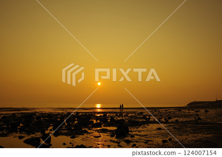 Ariake Sea, the morning sun, and the silhouette of two people walking on Takeshima Beach in Shimabara City at low tide 124007154