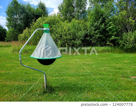 Horsefly trap against green trees. Photo of black ball insect trap on stand in mown meadow. Agricultural equipment for insect protection. Horsefly trap against green trees. Photo of black ball insect trap on stand in mown meadow. Agricultural equipment for insect protection. 124007778