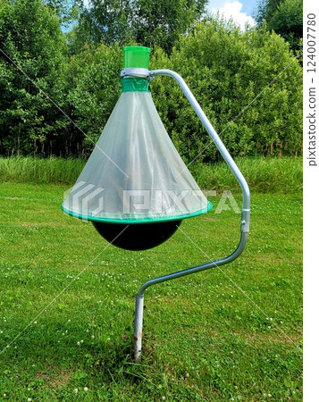 Horsefly trap against green trees. Photo of black ball insect trap on stand in mown meadow. Agricultural equipment for insect protection. Horsefly trap against green trees. Photo of black ball insect trap on stand in mown meadow. Agricultural equipment for insect protection. 124007780