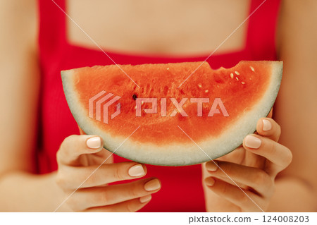 Close-up of well-groomed female manicured hands with a slice of juicy watermelon. A girl in a red T-shirt holds a piece of watermelon. Summer harvest. 124008203