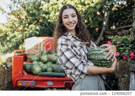 Charming smiling woman in casual clothes tosses watermelon outdoors 124008207