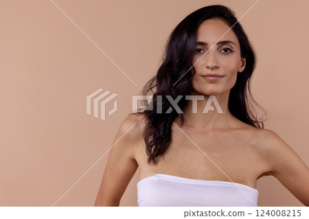 Studio portrait of a charming brunette woman in a white top with beautiful wavy hair and perfect skin. Studio portrait of a charming brunette woman in a white top with beautiful wavy hair and perfect skin. 124008215
