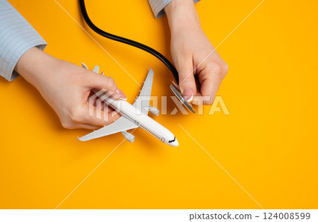 Passenger airplane and stethoscope in woman's hands. Concept of aviation industry and airline analysis. Aviation safety. Financial health of air travel businesses. Maintenance checks, travel risk 124008599