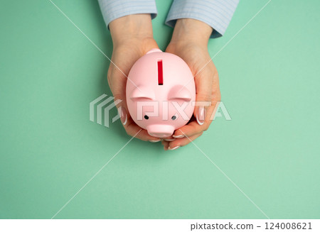 Piggy bank in woman's hands on turquoise background. Concept of savings and money accumulation. Accumulate bonuses. Saving strategies, managing personal finances. Budgeting, financial security. 124008621
