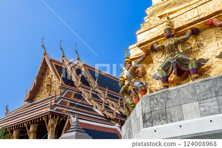 Yaksha guardian statues supporting a golden stupa at Wat Phra Kaew, Bangkok, Thailand. Ornate Thai temple architecture with intricate details and vibrant decorations. 124008968