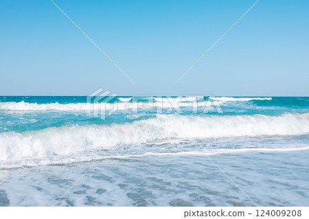 Mediterranean seascape. A picturesque sandy beach with turquoise waves gently rolling onto the shore. The azure sky, warm sand and sea foam create an atmosphere of calm and serenity 124009208