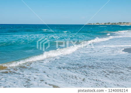 Mediterranean seascape. A picturesque sandy beach with turquoise waves gently rolling onto the shore. The azure sky, warm sand and sea foam create an atmosphere of calm and serenity 124009214