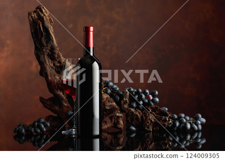 Bottle and glass of red wine with an old snag and blue grapes. Bottle and glass of red wine with an old snag and blue grapes. 124009305