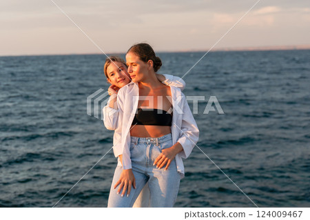 Women, Beach, Sunset. Two women pose on a beach with the ocean in the background during a sunset. 124009467