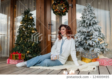 Woman Christmas Trees Decorated Porch Smiling woman sitting on a porch decorated for Christmas with two trees and presents. Woman Christmas Trees Decorated Porch Smiling woman sitting on a porch decorated for Christmas with two trees and presents. 124009495