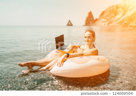 Woman laptop sea. Freelancer woman in sunglases floating on an inflatable big pink donut with a laptop in the sea. People summer vacation rest lifestyle concept 124009504