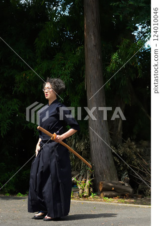一位身穿劍道服的老年婦女獨自在戶外用竹劍練習 124010046