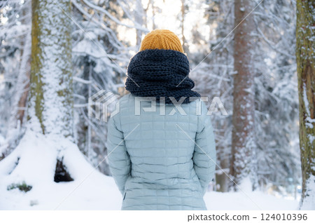 Young adult woman alone slowly walking on snow covered boardwalk after snowfall. Enjoying fresh air in park. Peaceful atmosphere in winter day. Back view Young adult woman alone slowly walking on snow covered boardwalk after snowfall. Enjoying fresh air in park. Peaceful atmosphere in winter day. Back view 124010396