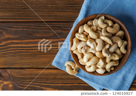 Cashew nuts presented in bowl placed on blue napkin on rustic wooden table, creating warm and inviting scene perfect for food and lifestyle imagery Cashew nuts presented in bowl placed on blue napkin on rustic wooden table, creating warm and inviting scene perfect for food and lifestyle imagery 124010927