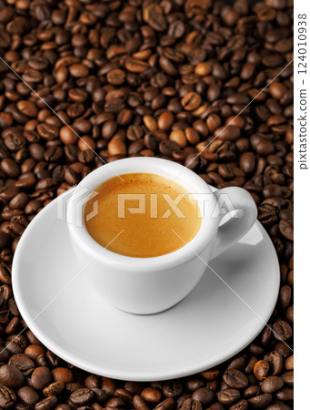 Small white espresso cup with saucer, nestled among bed of roasted coffee beans, creating cozy and inviting atmosphere perfect for enthusiasts 124010938
