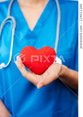 Close-up of a healthcare worker in blue scrubs holding a red heart, symbolizing compassion and care in the medical field. Close-up of a healthcare worker in blue scrubs holding a red heart, symbolizing compassion and care in the medical field. 124011160