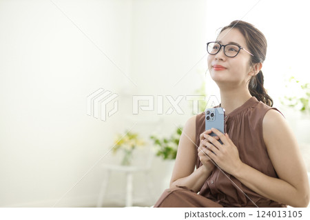 年輕女子坐在床上,看著她的智能手機 年輕女子坐在床上,看著她的智能手機 124013105